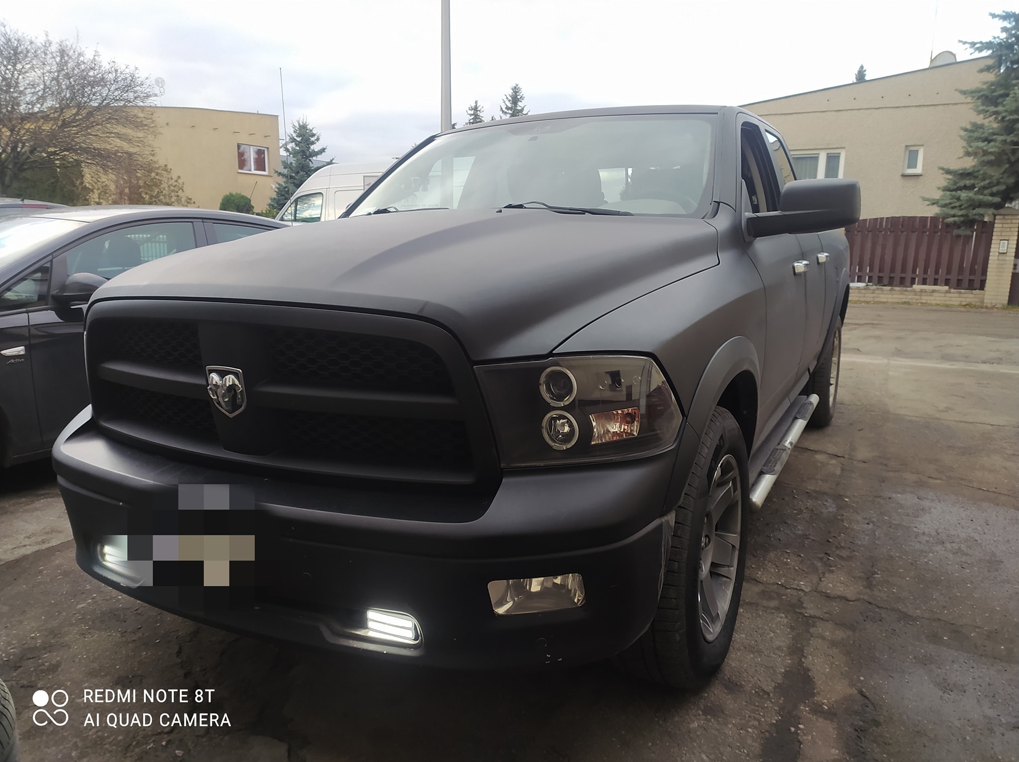 Czarny Dodge Ram po tuningu z ledowymi światłami dziennymi, zaparkowany przed budynkiem. Matowa karoseria, widoczne detale grilla i opon.