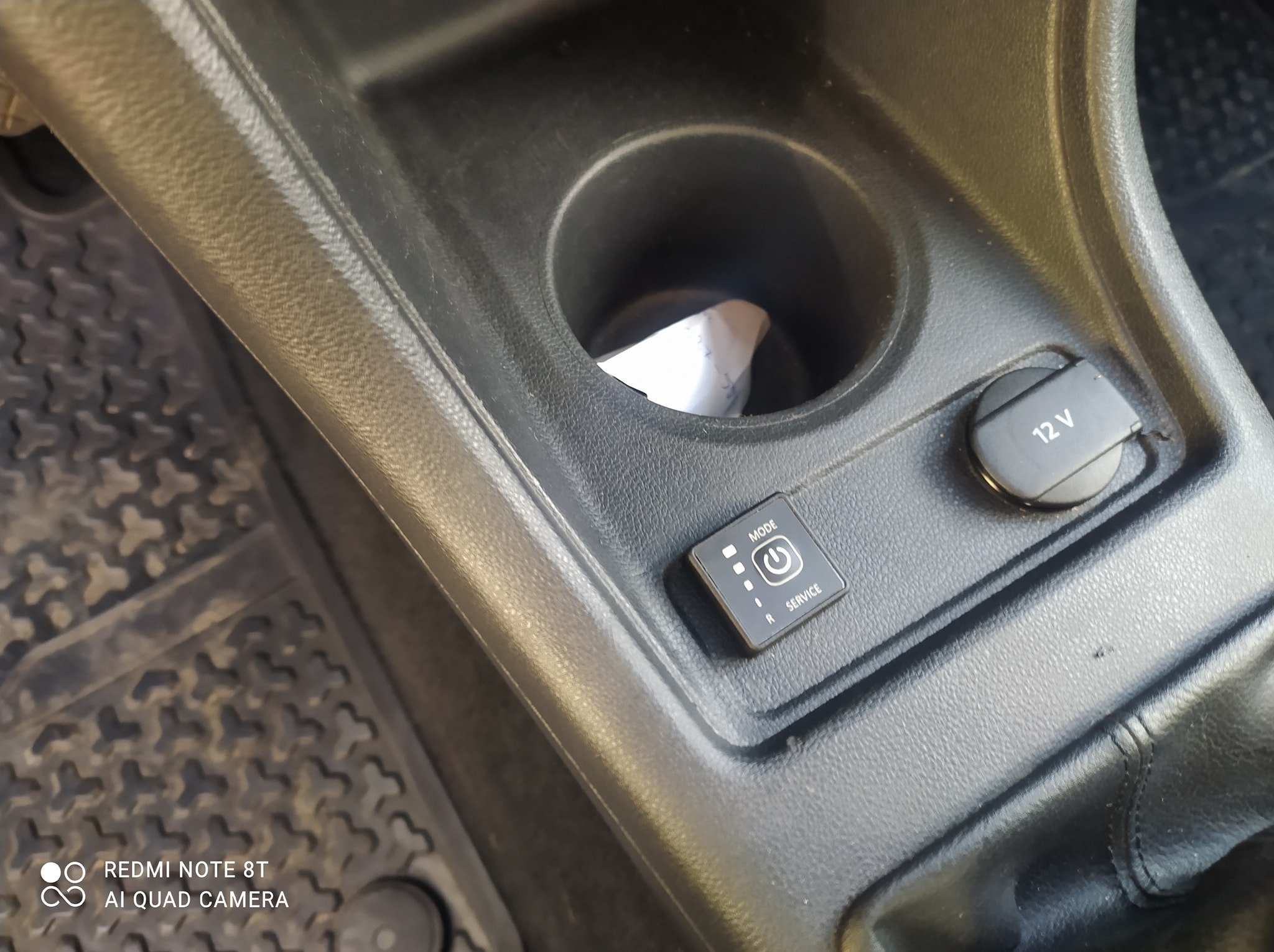 Panel sterowania LPG w samochodzie, umieszczony obok gniazda 12V i uchwytu na napoje. Widoczne detale wnętrza pojazdu.