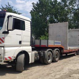 Orkan-Bud Sp z o.o. - Ciężarówka MAN z naczepą przewożąca betonowe prefabrykaty na tle zieleni, widok z boku, tablica 'Convoi Exceptionnel' na kabinie.