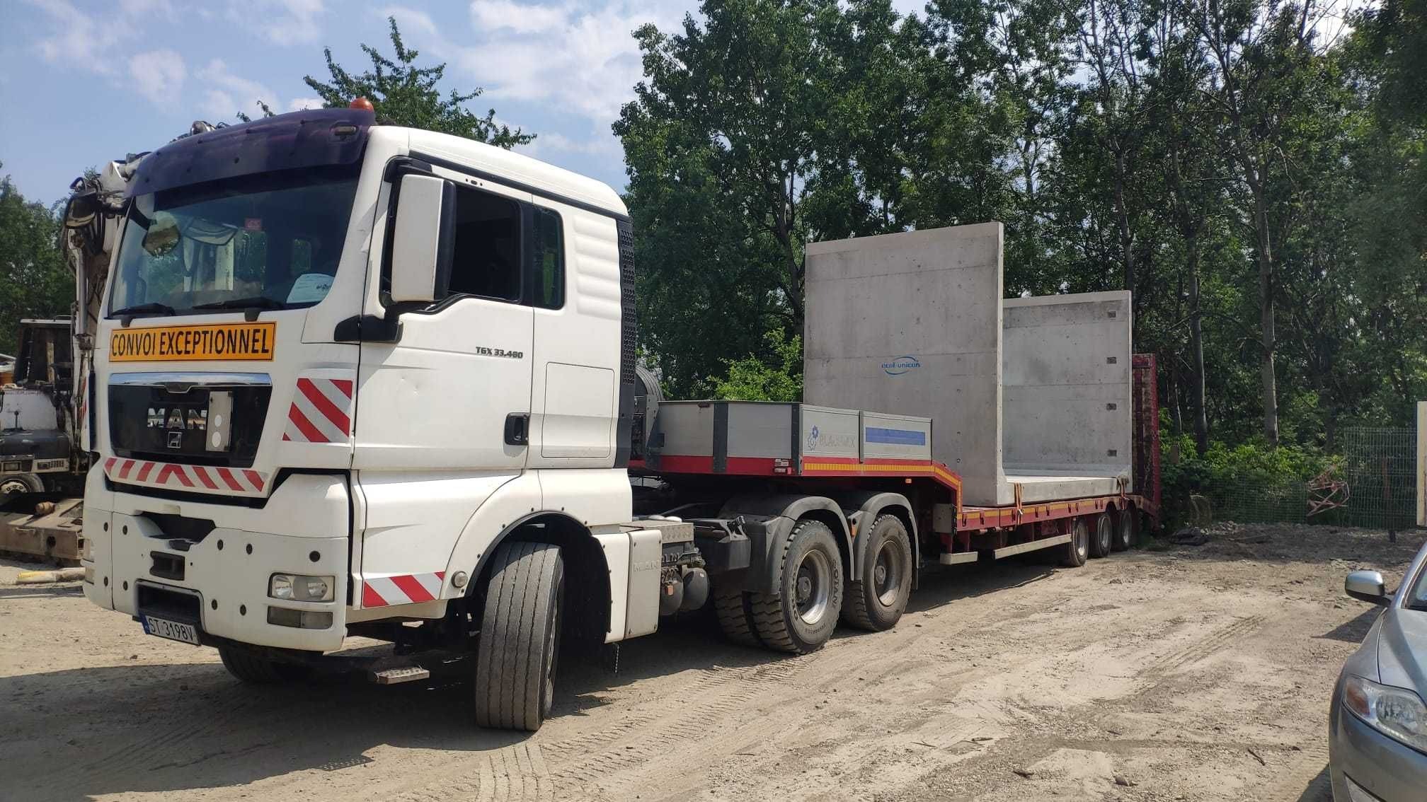 Ciężarówka MAN z naczepą przewożąca betonowe prefabrykaty na tle zieleni, widok z boku, tablica 'Convoi Exceptionnel' na kabinie.
