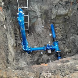 Wiert-Instal - Niebieskie rury połączone w wykopie ziemnym z drabiną, prawdopodobnie instalacja wodociągowa lub kanalizacyjna.