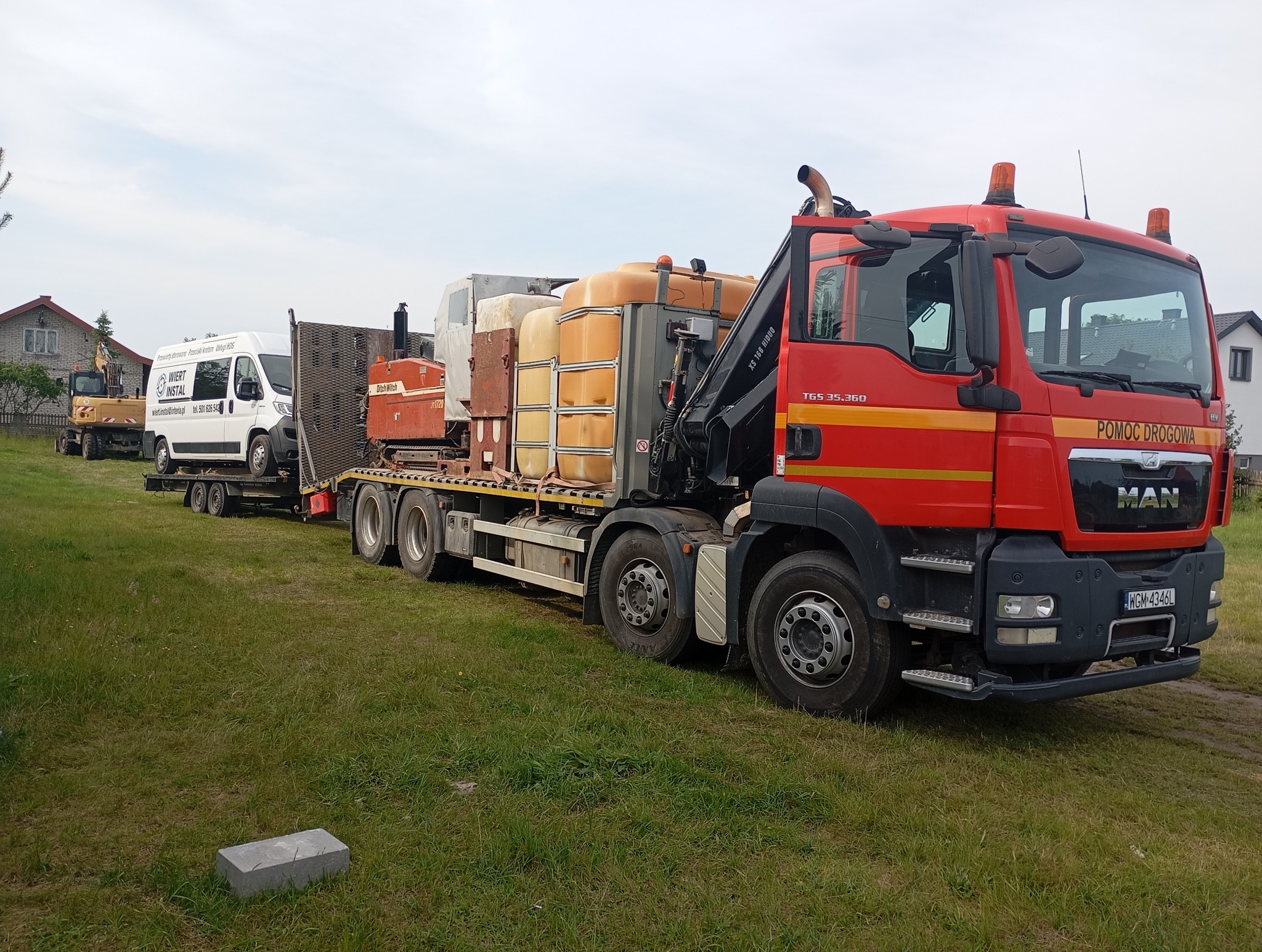Czerwony samochód ciężarowy MAN z napisem 'Pomoc Drogowa' transportuje sprzęt do przewiertów sterowanych, w tym Ditch Witch i biały bus z logo firmy Wiert Instal.