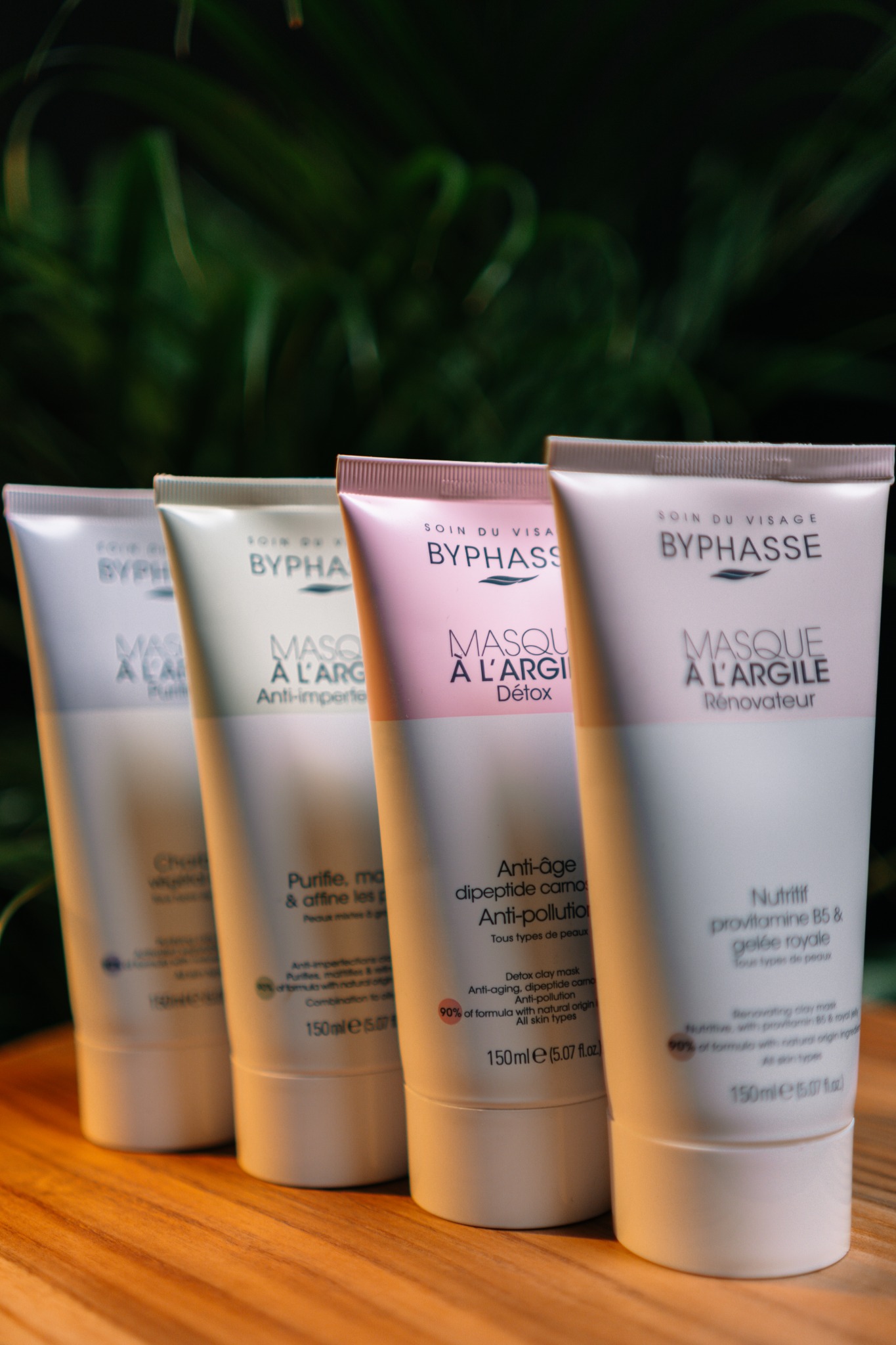 Cztery tuby maseczek do twarzy Byphasse z różnymi wariantami, ustawione na drewnianej powierzchni na tle zieleni, prezentujące produkty do pielęgnacji skóry.