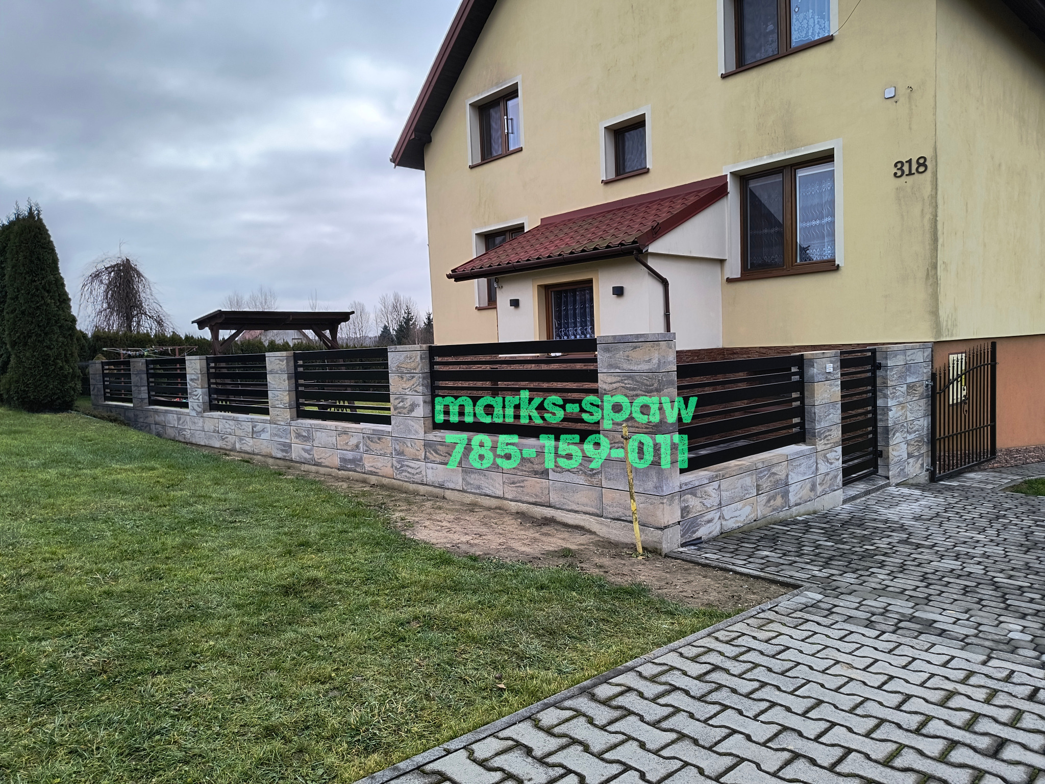 Nowoczesne ogrodzenie metalowe z kamiennymi słupkami, czarne poziome panele, brama wejściowa, dom w tle, trawnik. Widoczny numer domu 318.