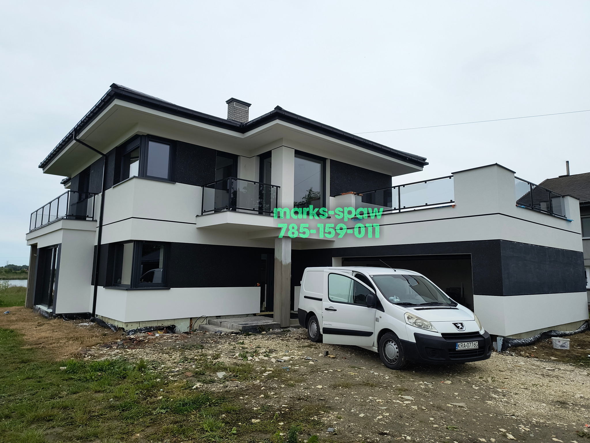 Nowoczesny dom z balkonami z balustradami szklanymi i czarnymi ramami okiennymi, biała bryła budynku z czarnymi akcentami, obok biały samochód dostawczy.