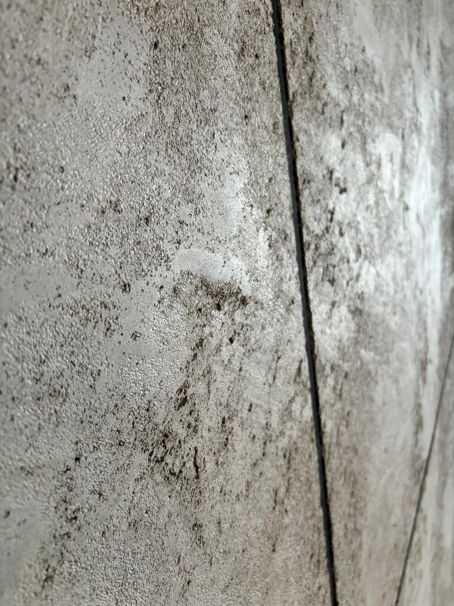 Szara, teksturowana ściana z widocznymi fugami, wykonana pod kątem, ukazująca nierówności i detale powierzchni. Dekoracyjna struktura ściany w zbliżeniu.