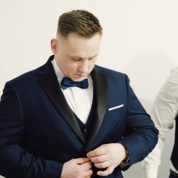 Studio Filmowe Trwaj Chwilo - Mężczyzna w granatowym smokingu zapina guzik, obok drugi mężczyzna w kamizelce i muszce. Przygotowania do uroczystości, elegancki strój.