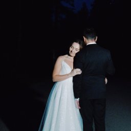 Studio Filmowe Trwaj Chwilo - Para młoda w nocnej scenerii: panna młoda w sukni z brokatem opiera się o pana młodego w ciemnym garniturze. Romantyczny kadr w głębokiej czerni.