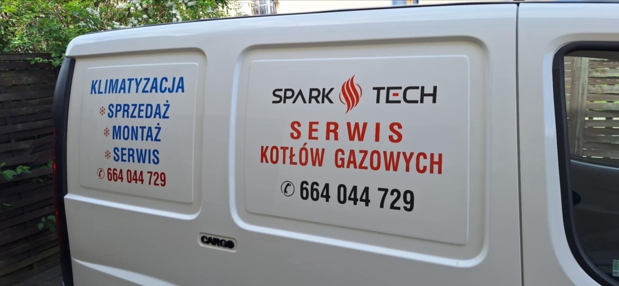 Biały samochód dostawczy z reklamą usług: klimatyzacja (sprzedaż, montaż, serwis) i serwis kotłów gazowych Spark Tech, numer telefonu.
