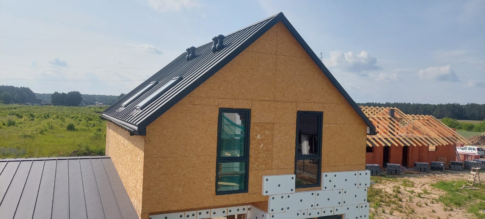 Budowa domu szkieletowego z czarnym dachem w Opolu. Widoczne okna dachowe i elewacja z płyt OSB. Częściowo ocieplona podstawa budynku.