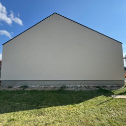 Elewarm - Ściana domu po tynkowaniu na gładko, widoczne rusztowanie z boku, trawa i niebieskie niebo. Minimalistyczny design elewacji.