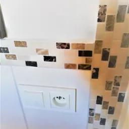 Wykończenie ściany mozaiką z elementami imitującymi marmur, gniazdko elektryczne i włącznik światła na białej ścianie. Ukończony etap prac wykończeniowych.