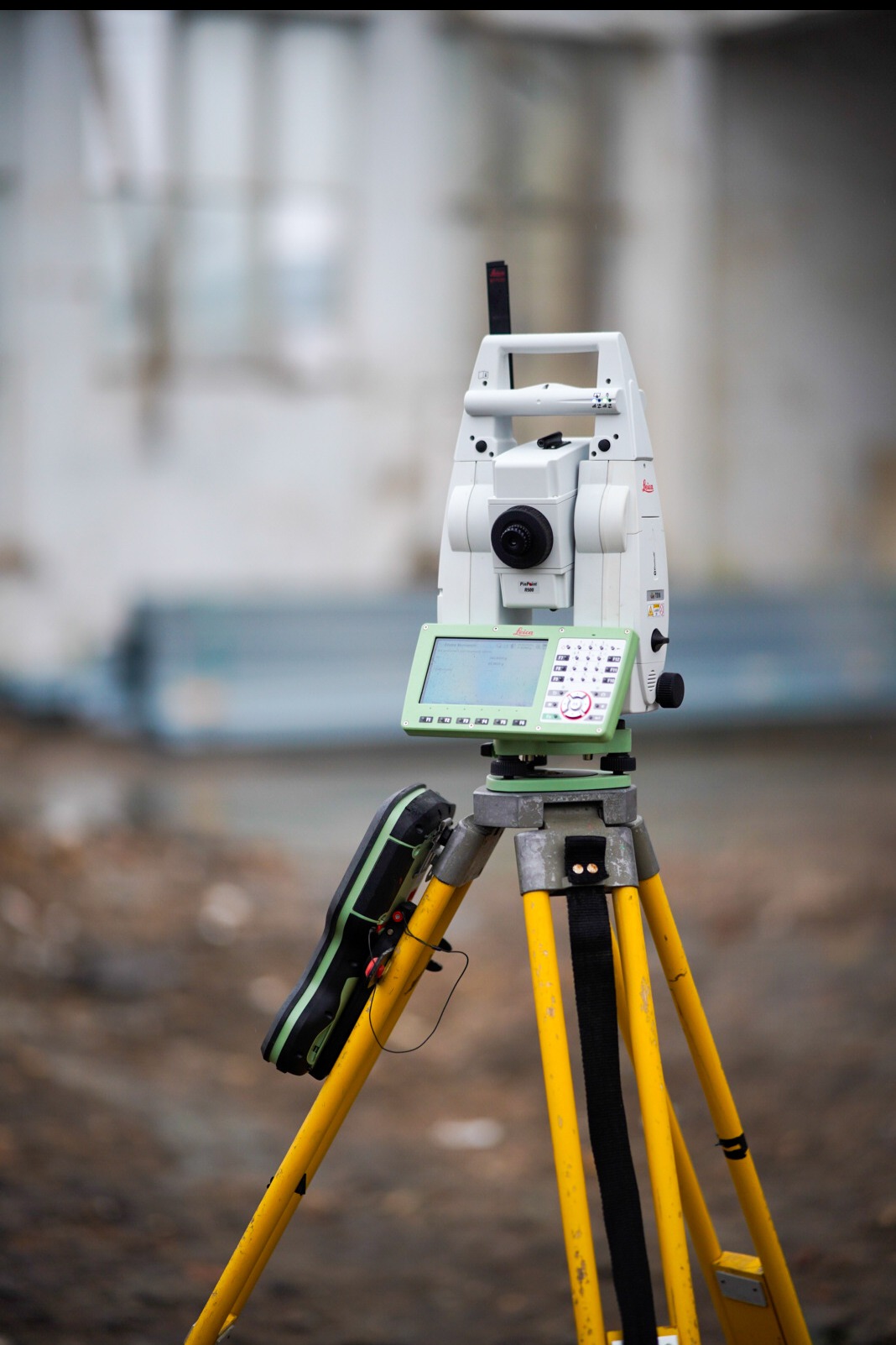 Profesjonalny, biały tachimetr Leica na żółtym statywie w terenie. Ekran urządzenia z mapą. Sprzęt pomiarowy gotowy do pracy.