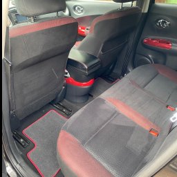 Bartłomiej karolak - Wnętrze samochodu z czarno-czerwonymi akcentami: tylne siedzenia i dywaniki po czyszczeniu, widoczne detale wykończenia, welurowa tapicerka.