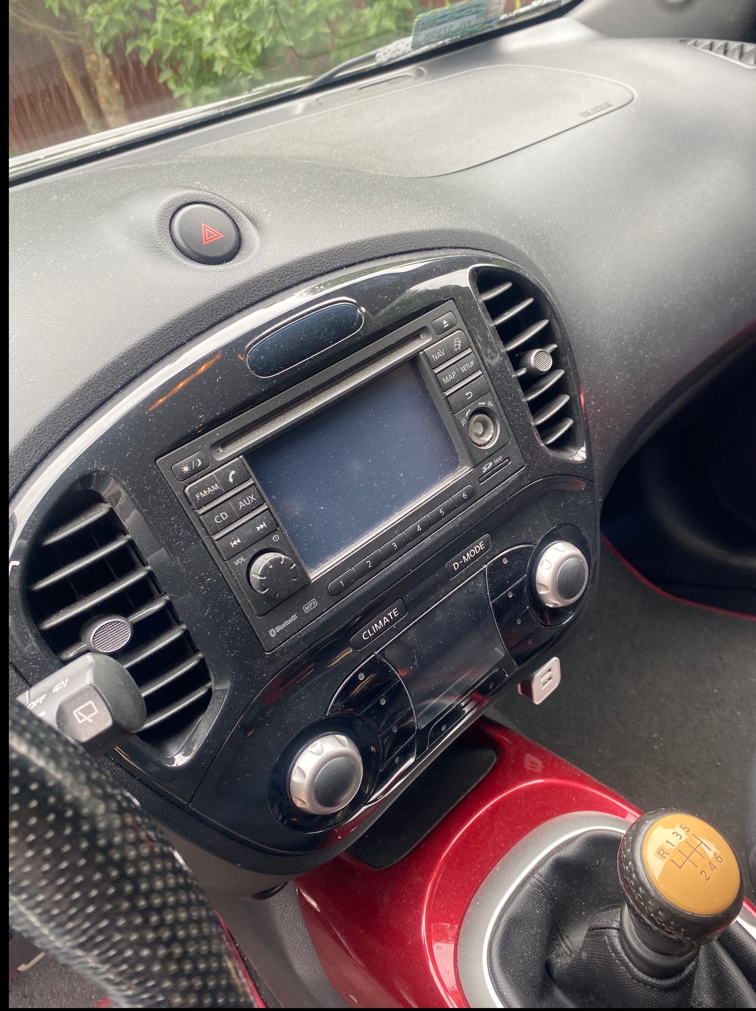 Brudna deska rozdzielcza i panel sterowania klimatem w samochodzie Nissan Juke. Widoczny kurz i zabrudzenia na powierzchniach. Gałka zmiany biegów w kolorze żółtym.