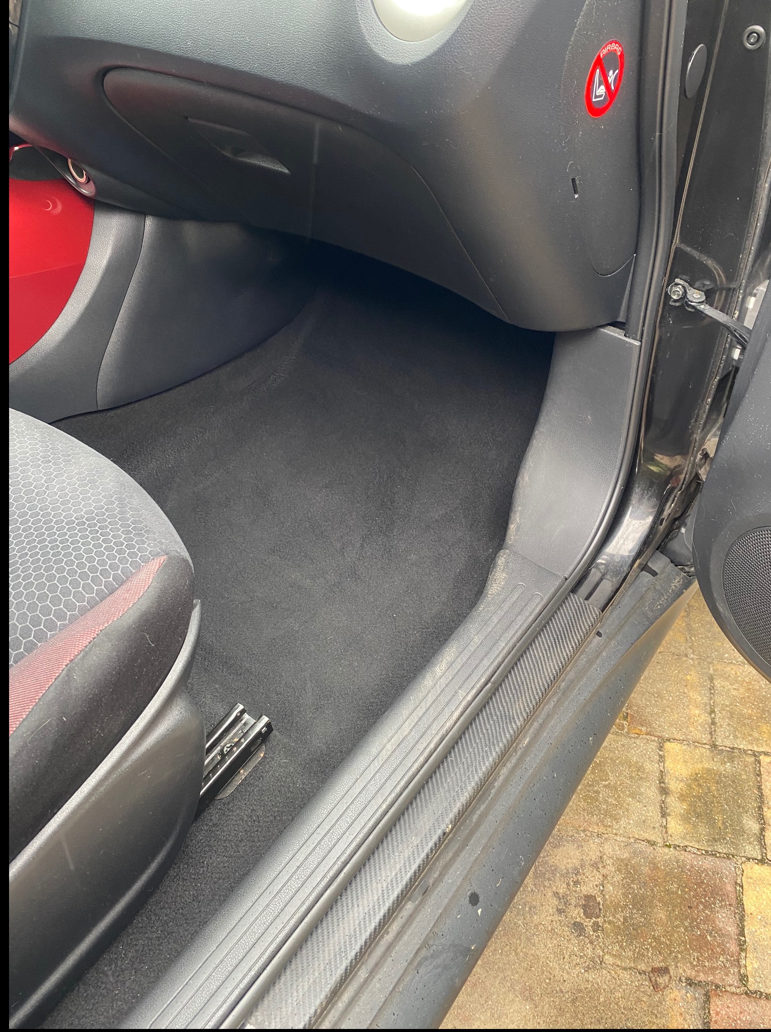 Wnętrze czarnego samochodu po praniu tapicerki, widoczne czyste dywaniki i podłoga, z detalami deski rozdzielczej i siedzenia kierowcy.