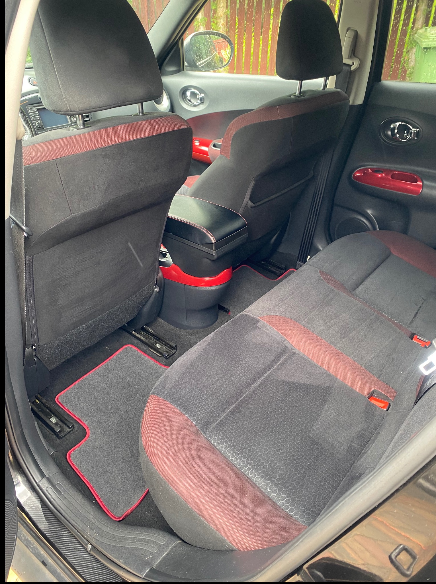 Wnętrze samochodu z czarno-czerwonymi akcentami: tylne siedzenia i dywaniki po czyszczeniu, widoczne detale wykończenia, welurowa tapicerka.