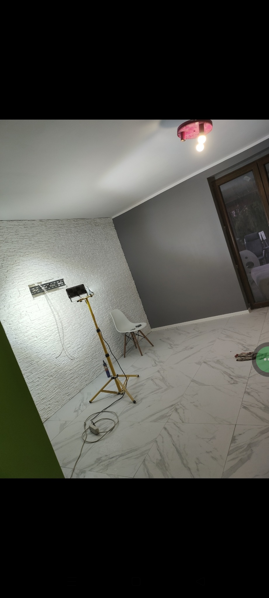 Pokój po remoncie z białymi płytkami imitującymi cegłę na ścianie, marmurowe płytki podłogowe i lampa na statywie. Ściana pomalowana na szaro.