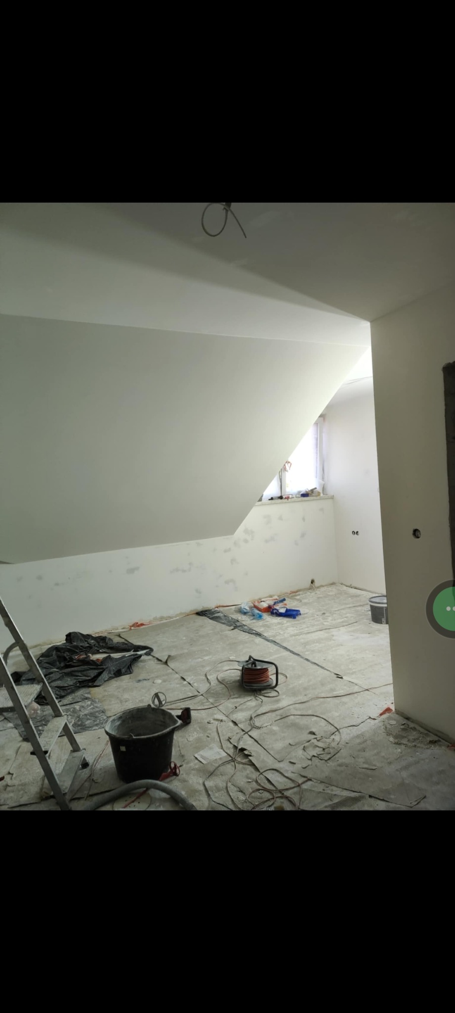 Pokój na poddaszu w trakcie gładziowania ścian i sufitu. Widoczne narzędzia: drabina, wiadro, szlifierka. Ściany przygotowane pod malowanie, z widocznymi śladami szpachlowania.