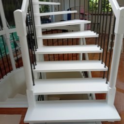 Białe, odnowione schody spiralne z czarnymi balustradami w Toruniu. Widok z dołu, ukazujący detale wykończenia i drewnianą podłogę.