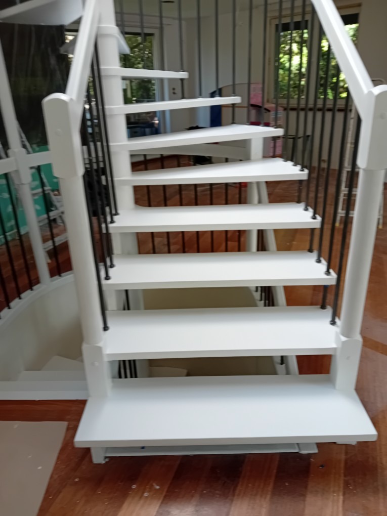 Białe, odnowione schody spiralne z czarnymi balustradami w Toruniu. Widok z dołu, ukazujący detale wykończenia i drewnianą podłogę.