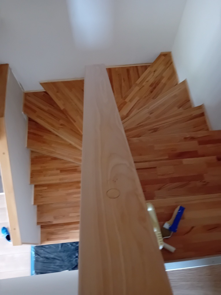 Spiralne schody z jasnego drewna po cyklinowaniu, widok z góry. Na dole widoczne narzędzia i zabezpieczenia podłogi. Charakterystyczny wzór ułożenia desek.