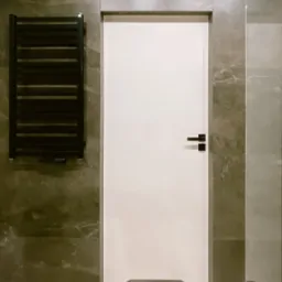 Nowoczesna łazienka z białą, minimalistyczną stolarką drzwiową, grafitowymi płytkami imitującymi marmur i czarnym grzejnikiem drabinkowym.