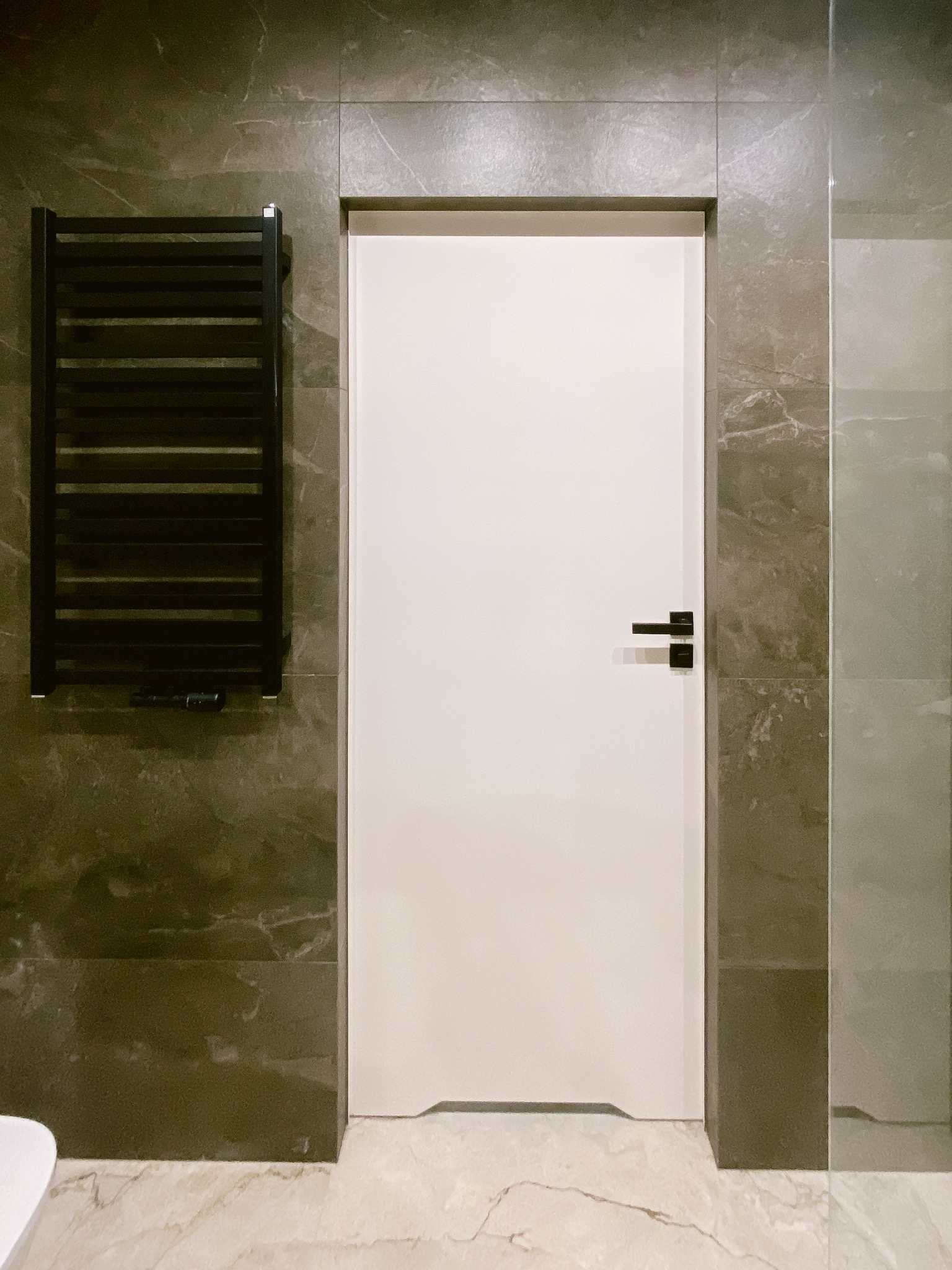 Nowoczesna łazienka z białą, minimalistyczną stolarką drzwiową, grafitowymi płytkami imitującymi marmur i czarnym grzejnikiem drabinkowym.