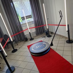 Fabryka Uśmiechu i Mebli David Parma - Rozstawiona fotobudka 360 z oświetleniem LED i czerwonym dywanem, przygotowana do użycia. W tle okno z szarymi zasłonami i białą firanką.