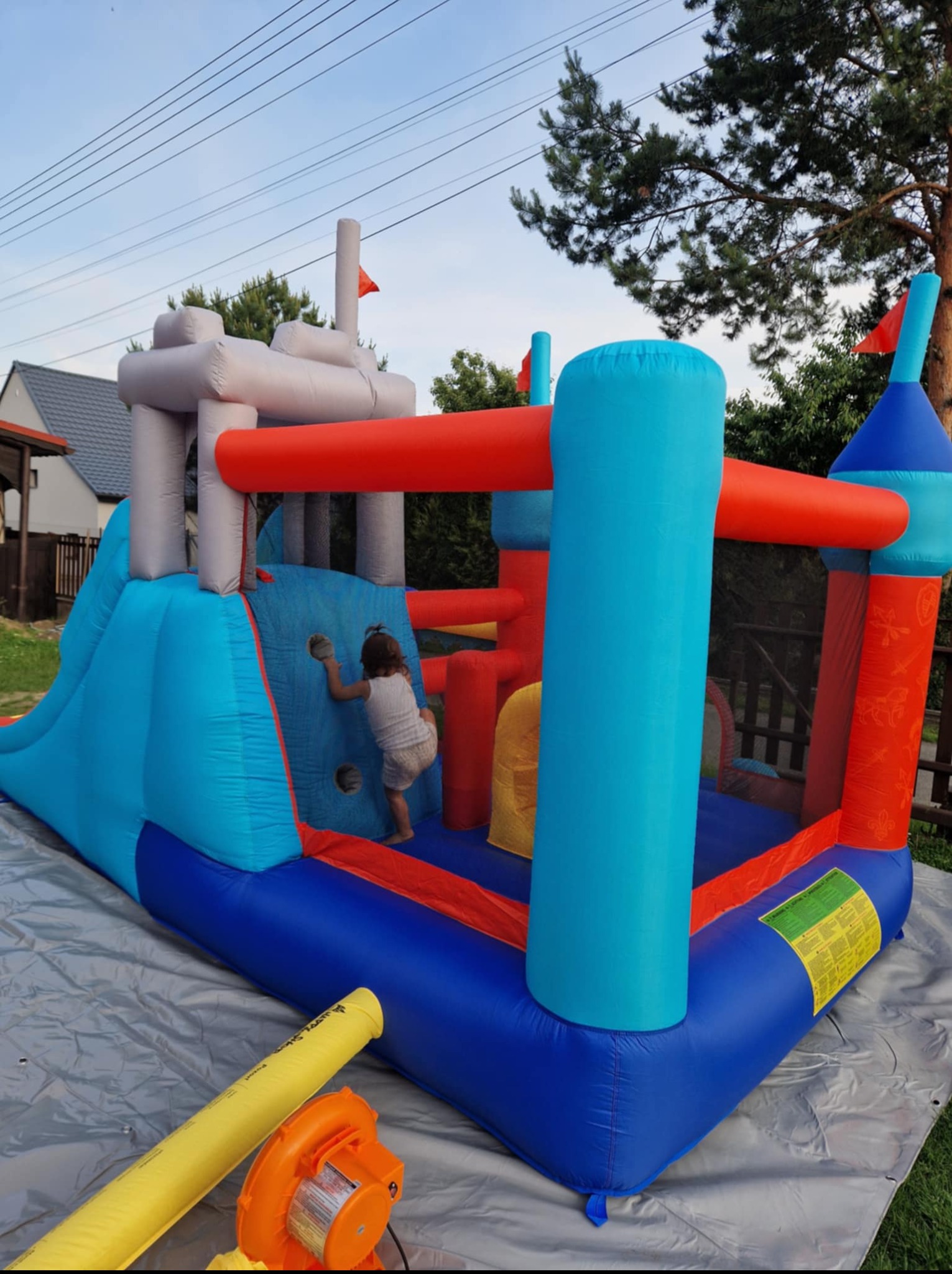 Kolorowy dmuchany zamek z tunelem i zjeżdżalnią w Gorzyczkach, z dzieckiem wspinającym się po ściance. Widoczny wentylator do pompowania.