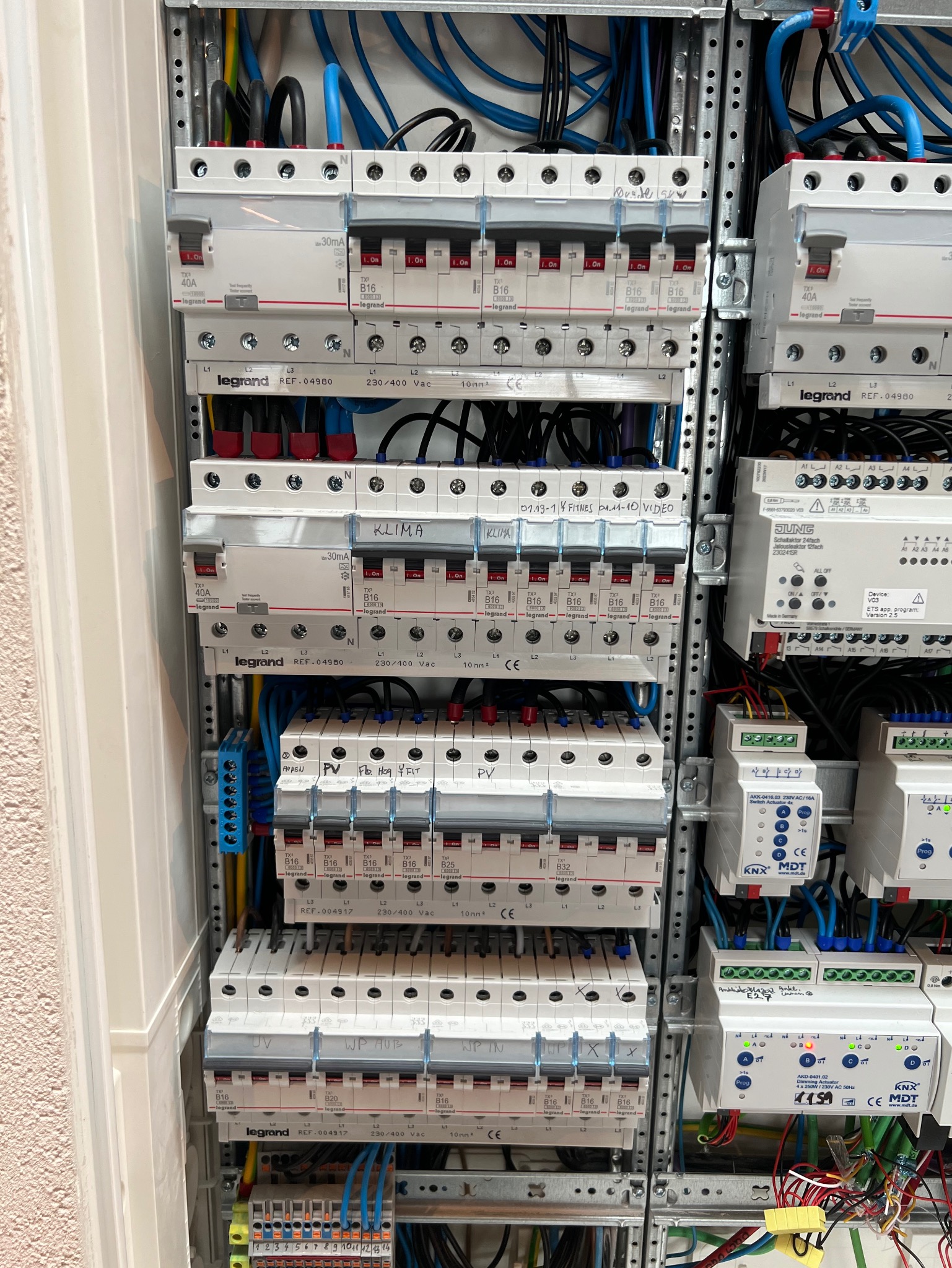 Rozdzielnica elektryczna z bezpiecznikami Legrand, okablowaniem i modułami KNX MDT. Widoczne opisy obwodów: Klima, PV, Video, Fitness. Instalacja w obudowie.