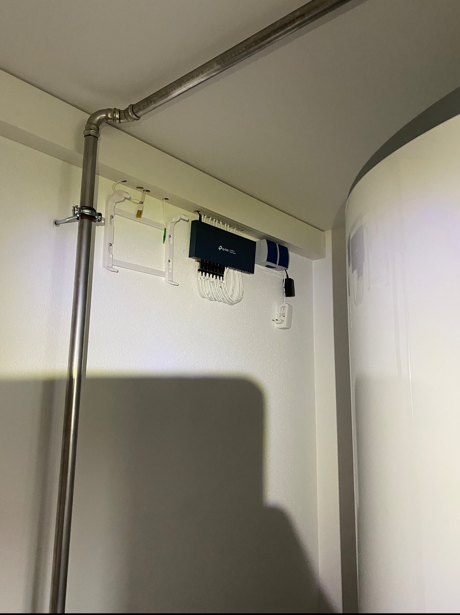 Centrala rekuperacyjna TP-Link w białym pomieszczeniu. Widoczna rura instalacyjna i biały zbiornik. Kompaktowe rozwiązanie z podłączeniami.