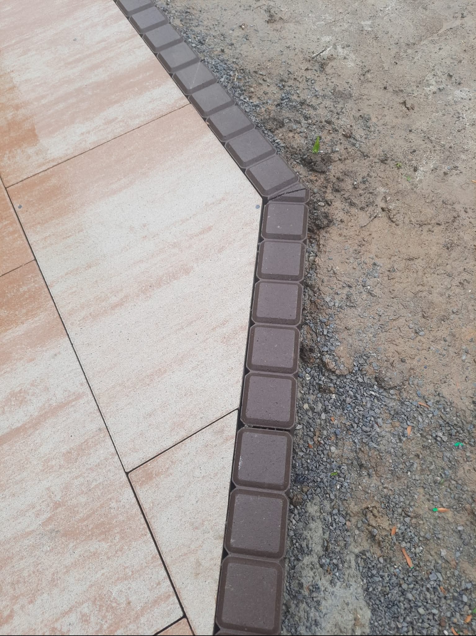 Ułożona jasna kostka brukowa z obrzeżem z ciemnej kostki, widok z góry, fragment terenu z drobnym żwirem.