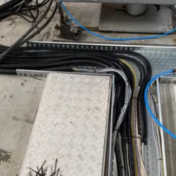 Ułożone kable w korytkach instalacyjnych z narzędziami i wiązkami kablowymi, widoczne przewody w różnych kolorach i średnicach.