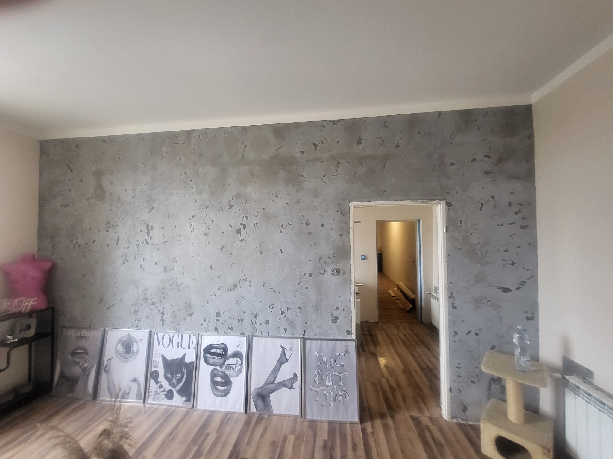 Ściana z efektem dekoracyjnym w szarościach, widoczne grafiki w ramkach, drewniana podłoga, wnętrze po wykończeniu, z widokiem na kolejne pomieszczenie.
