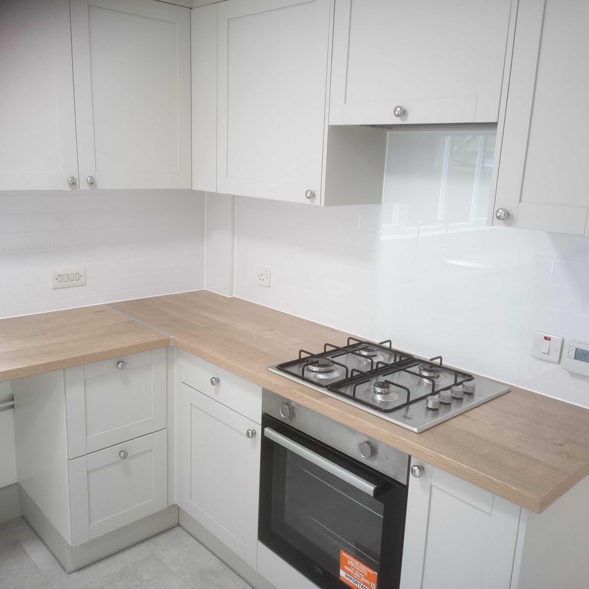 Jasna kuchnia z drewnianym blatem, płytą gazową i piekarnikiem. Białe szafki z chromowanymi uchwytami. Na ścianie białe płytki imitujące cegłę.