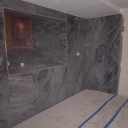 Erbeer - Wykończona łazienka z szarymi płytkami imitującymi marmur na ścianach, widoczne zabezpieczenie podłogi taśmą malarską. Wnęka z oświetleniem.