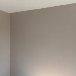 Świeżo pomalowane ściany w odcieniach beżu i bieli, widoczne łączenie ścian i sufitu, fragment drewnianej podłogi. Minimalistyczne wykończenie wnętrza.