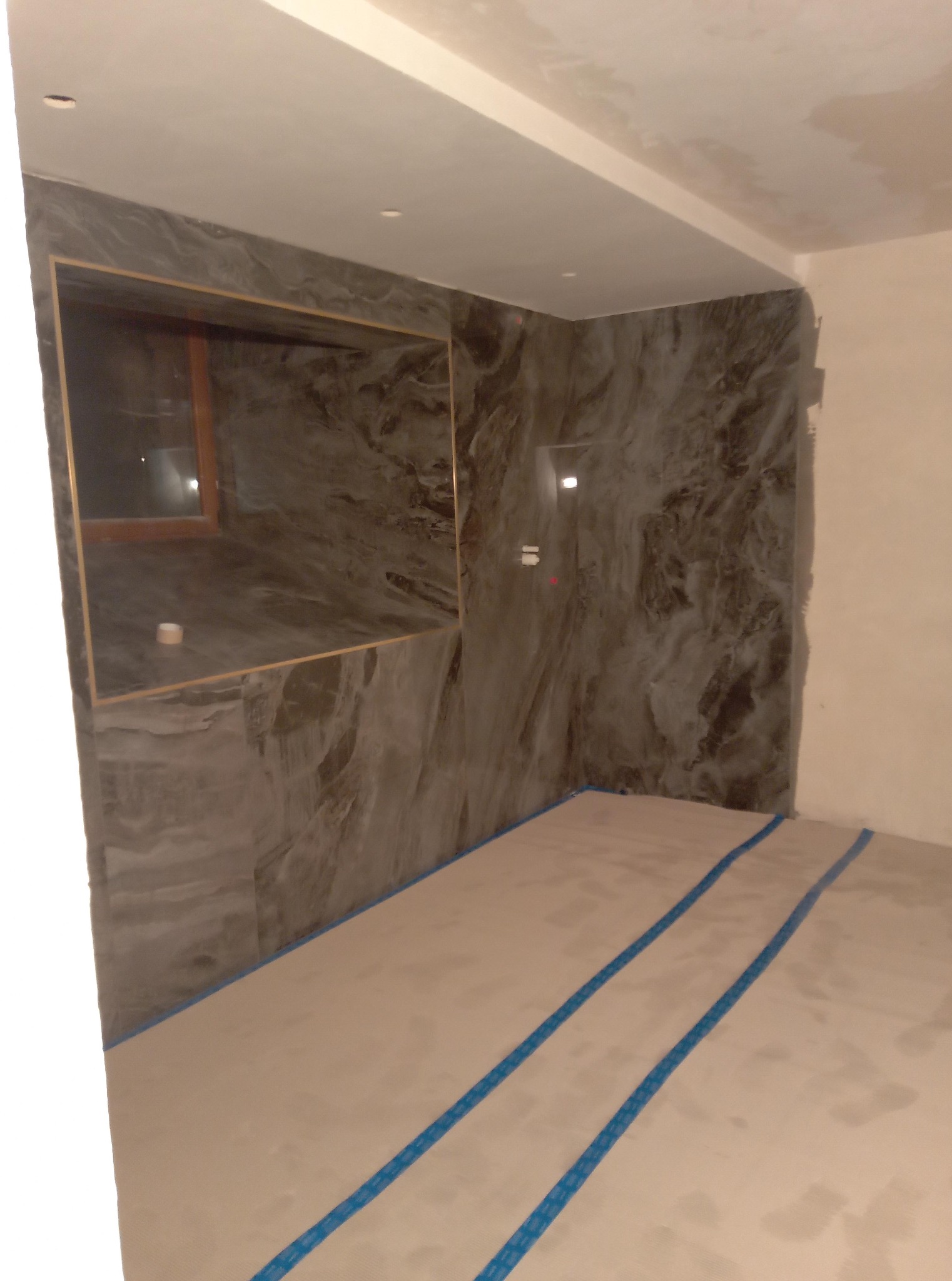 Wykończona ściana z szarego marmuru z wnęką w łazience, zabezpieczona podłoga przed dalszymi pracami wykończeniowymi w pomieszczeniu.
