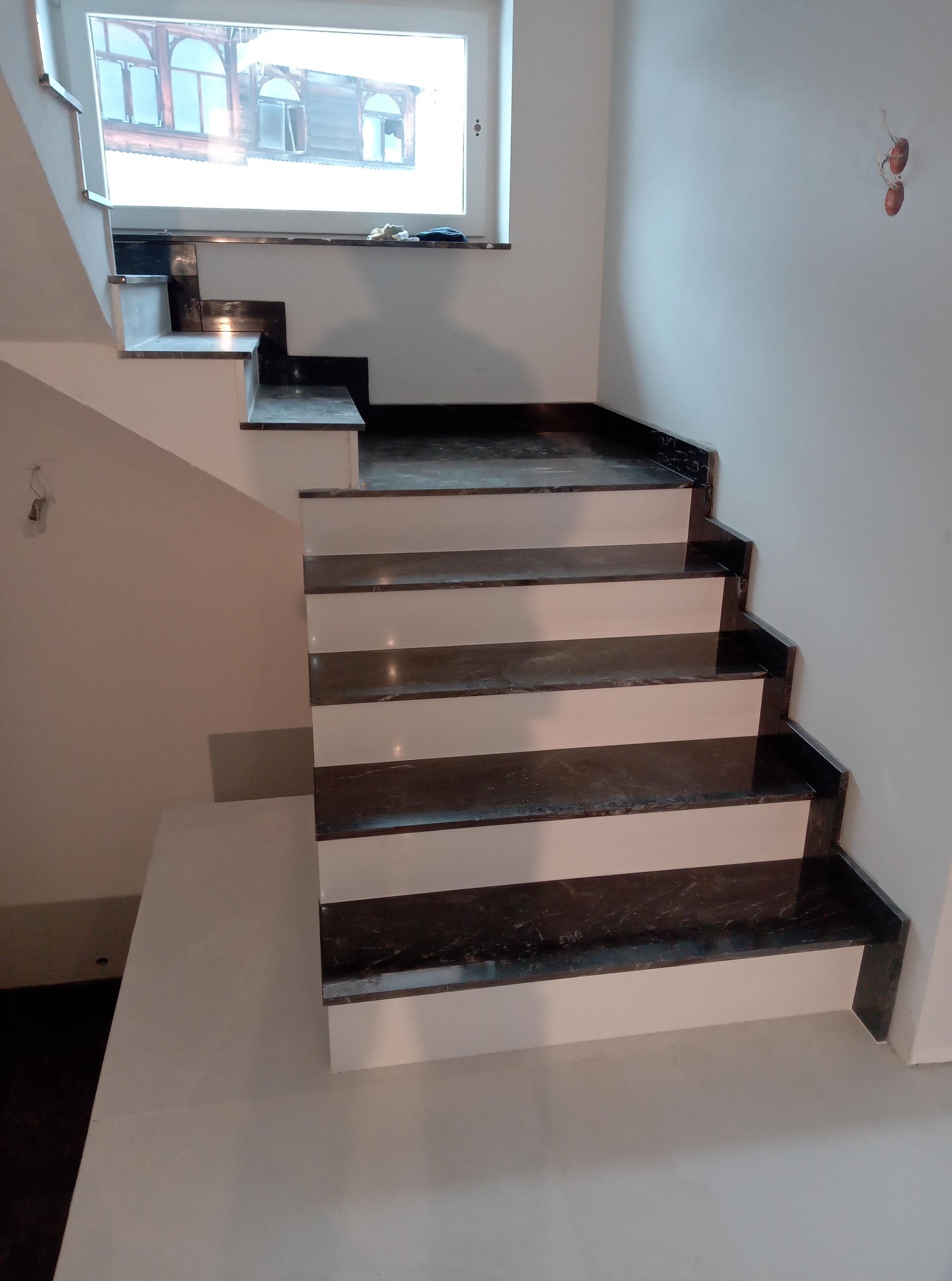 Schody wewnętrzne z ciemnego marmuru z białymi podstopnicami, wykończone w nowoczesnym stylu. Widoczne detale wykończenia i oświetlenie.