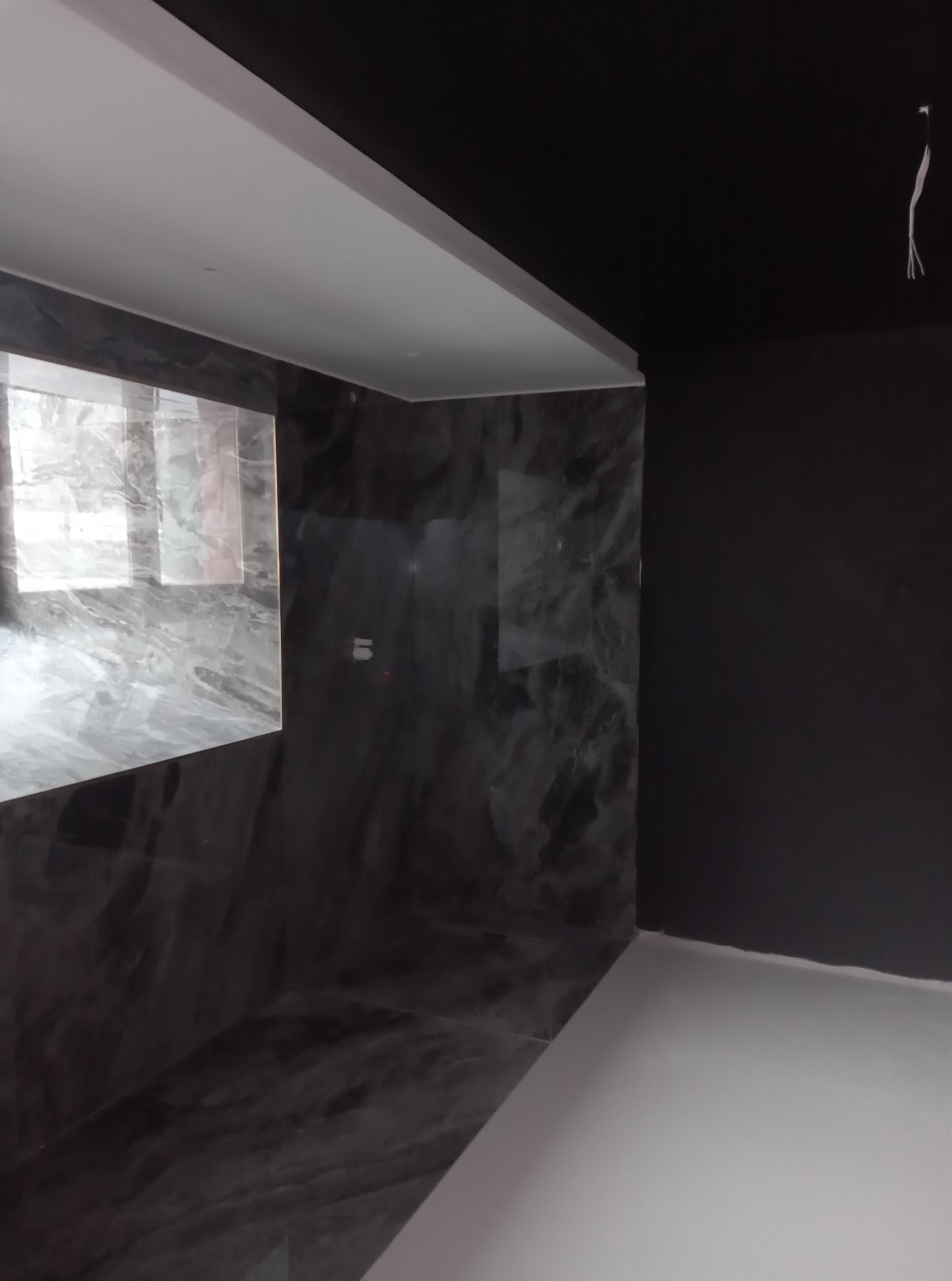 Wykończone wnętrze: ściany w ciemnym marmurze, biały sufit z listwą i czarny sufit w głębi. Widoczne kable. Minimalistyczny design, nowoczesne wykończenie.