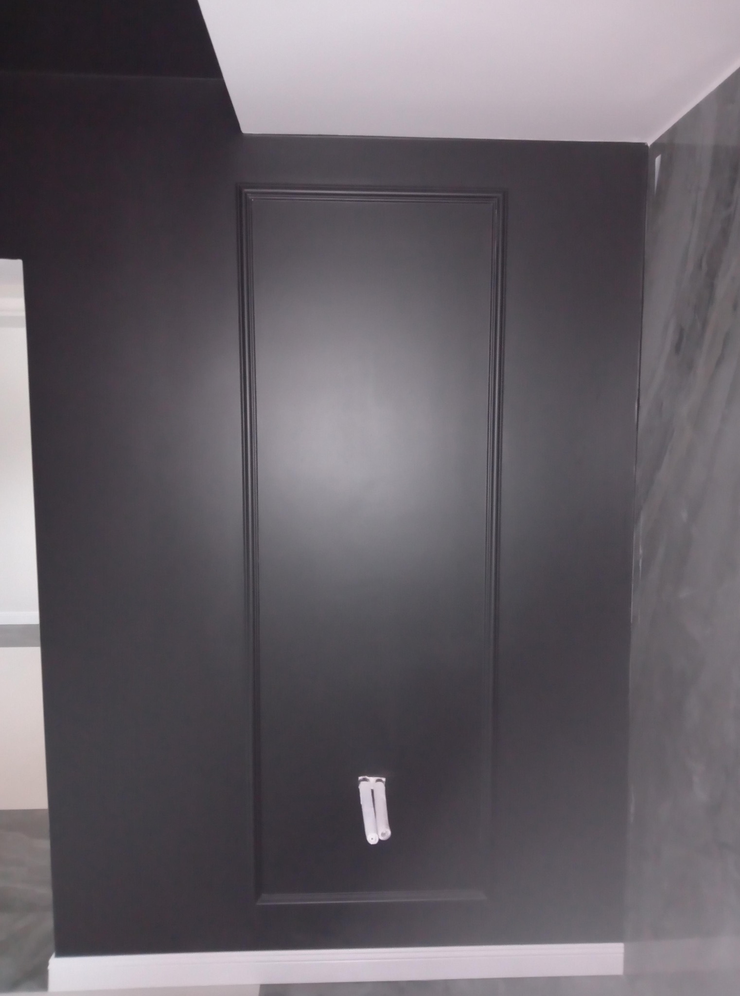 Ciemna ściana z dekoracyjną ramą i wystającymi przewodami w Brzozowie. Minimalistyczny design wnętrza, fragment marmurowej ściany po prawej stronie.