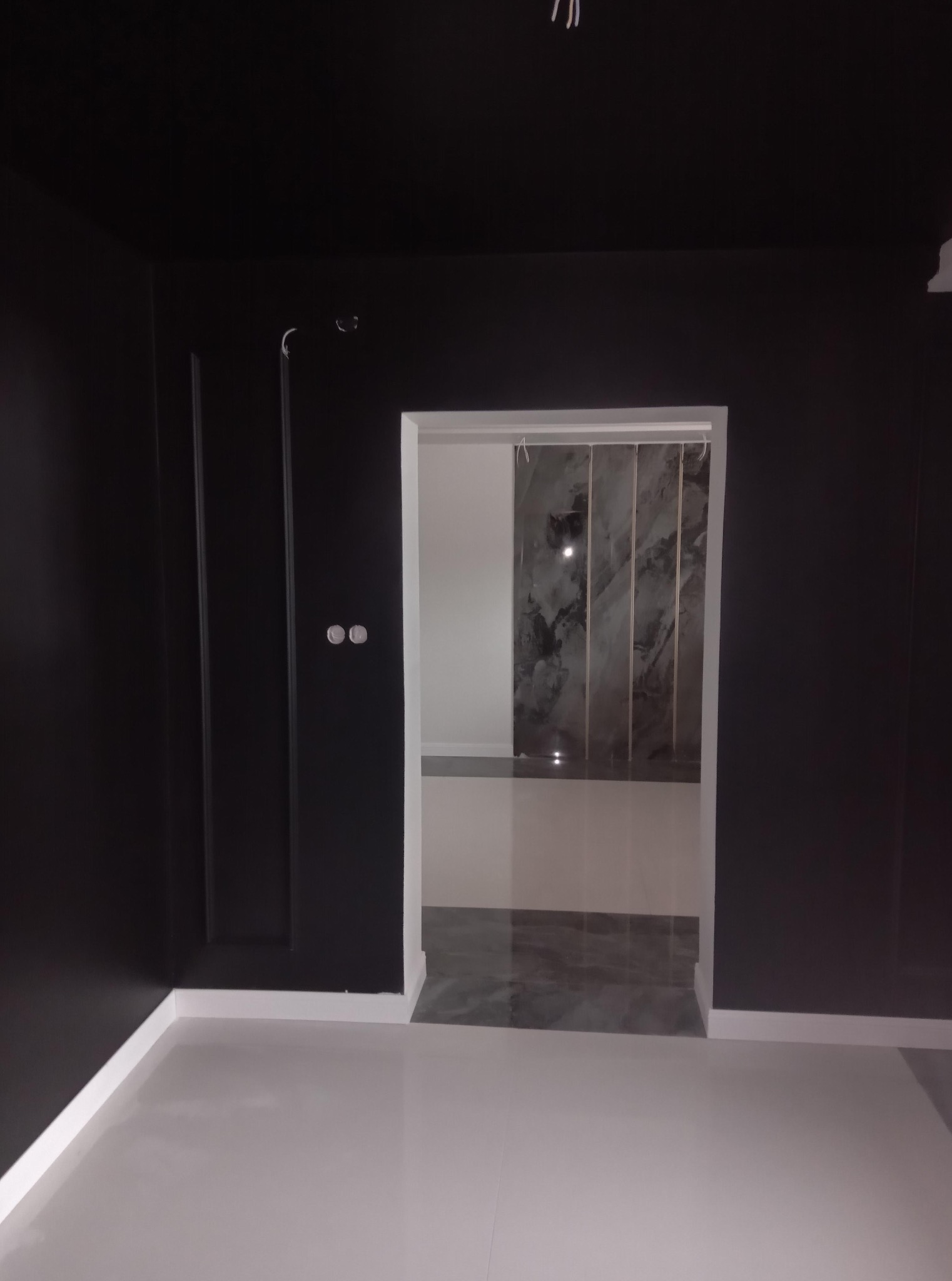 Czarne ściany z dekoracyjnymi listwami i białymi podłogami. W głębi widoczna marmurowa ściana w łazience. Minimalistyczny design wnętrza po remoncie.