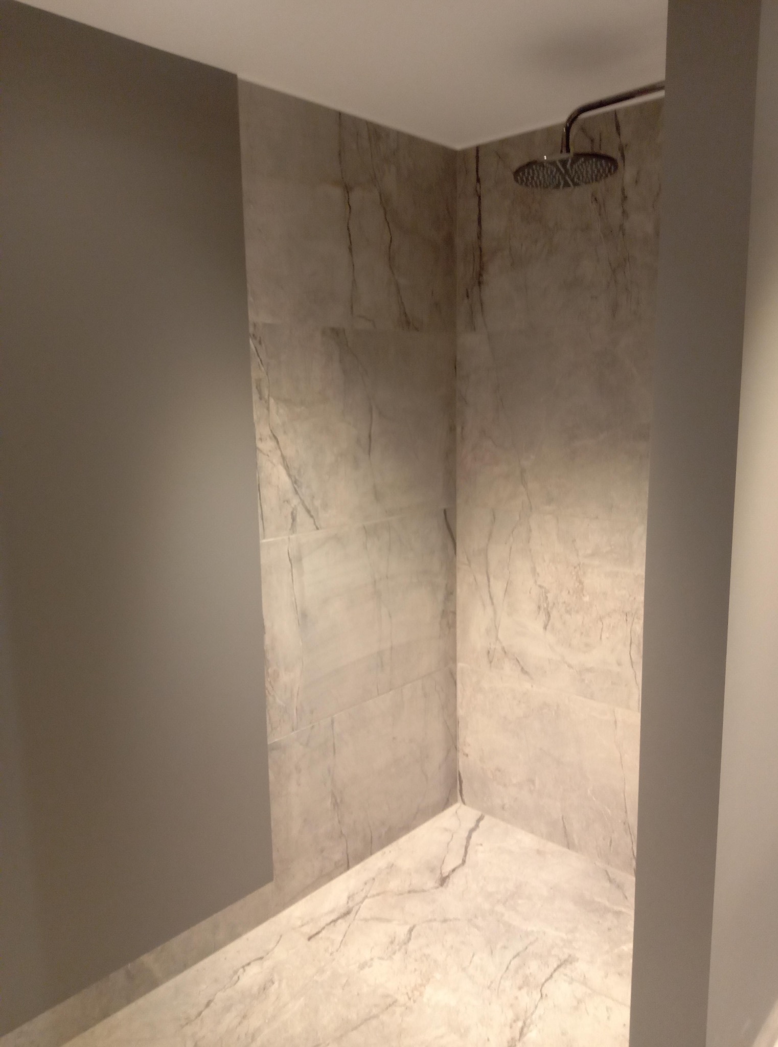 Wykończona kabina prysznicowa z marmurowymi płytkami na ścianach i podłodze, widoczna deszczownica. Szara ściana kontrastuje z jasnym wykończeniem.