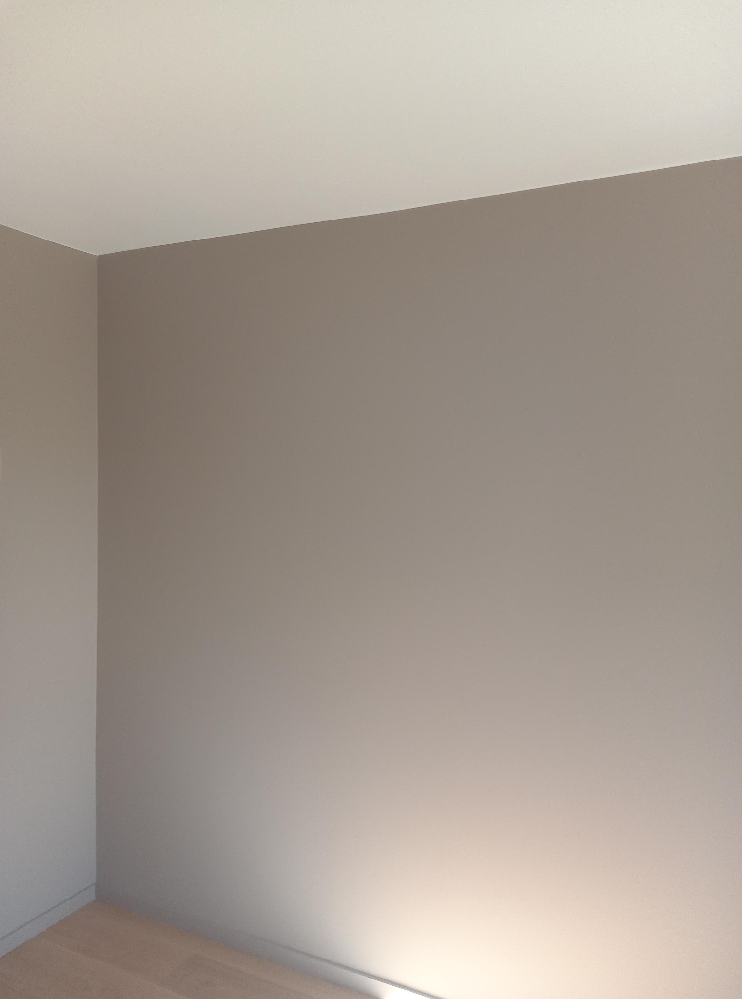 Świeżo pomalowane ściany w odcieniach beżu i bieli, widoczne łączenie ścian i sufitu, fragment drewnianej podłogi. Minimalistyczne wykończenie wnętrza.