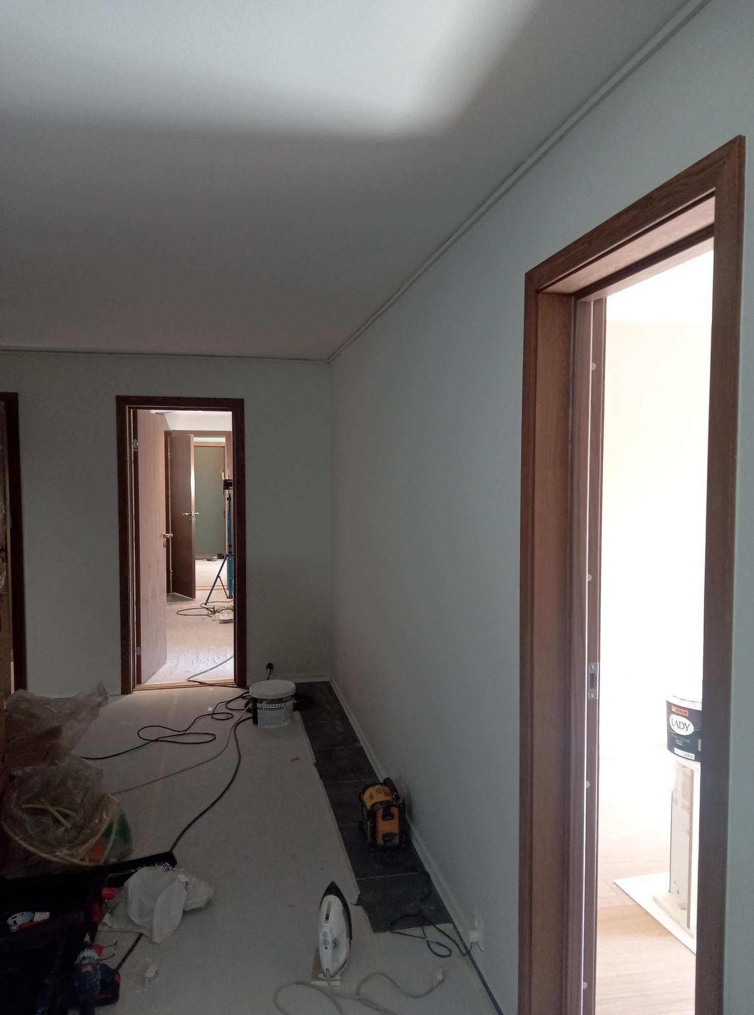 Wnętrze w trakcie malowania ścian na biało. Widoczne zabezpieczone podłogi, puszka z farbą Jotun Lady i narzędzia malarskie. Ościeżnice w kolorze drewna.