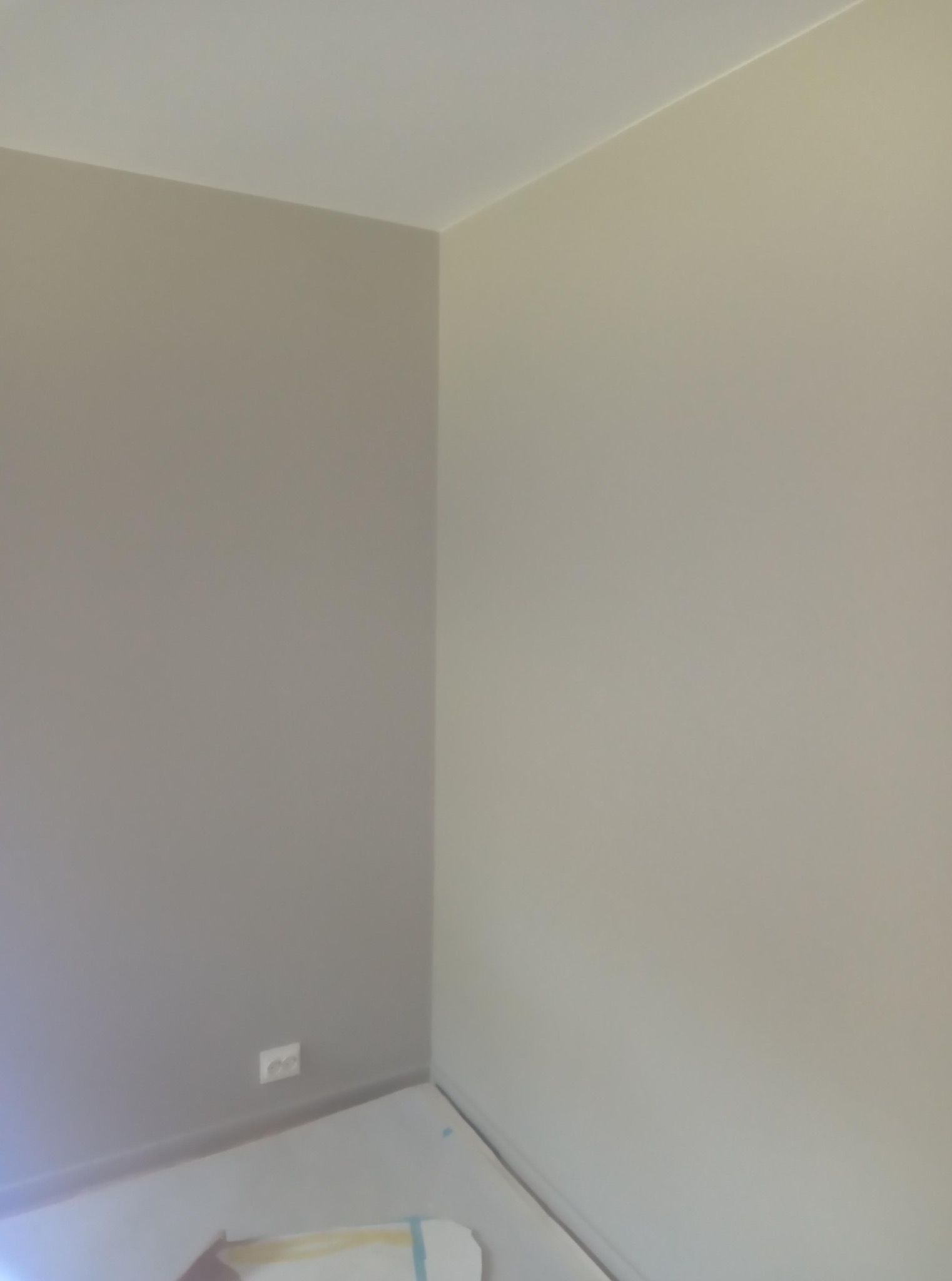 Pomieszczenie po szpachlowaniu i malowaniu na dwa odcienie szarości, z widocznym gniazdkiem elektrycznym przy podłodze. Ściany gładkie, gotowe do dalszych prac wykończeniowych.