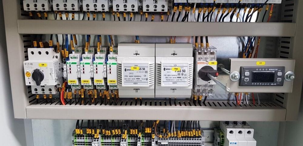 Rozdzielnia elektryczna z widocznymi zabezpieczeniami, transformatorami i sterownikiem temperatury. Przewody uporządkowane w listwach.