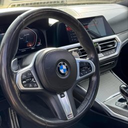 PROSHINE - Wnętrze luksusowego BMW z czarną skórzaną tapicerką i kierownicą. Widoczne detale deski rozdzielczej i ekran dotykowy. Elementy wykończenia w kolorze srebrnym.