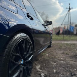 PROSHINE - Błyszczący, granatowy samochód BMW po umyciu, z bliska widoczne czyste felgi na tle pochmurnego nieba i wiejskiego krajobrazu.
